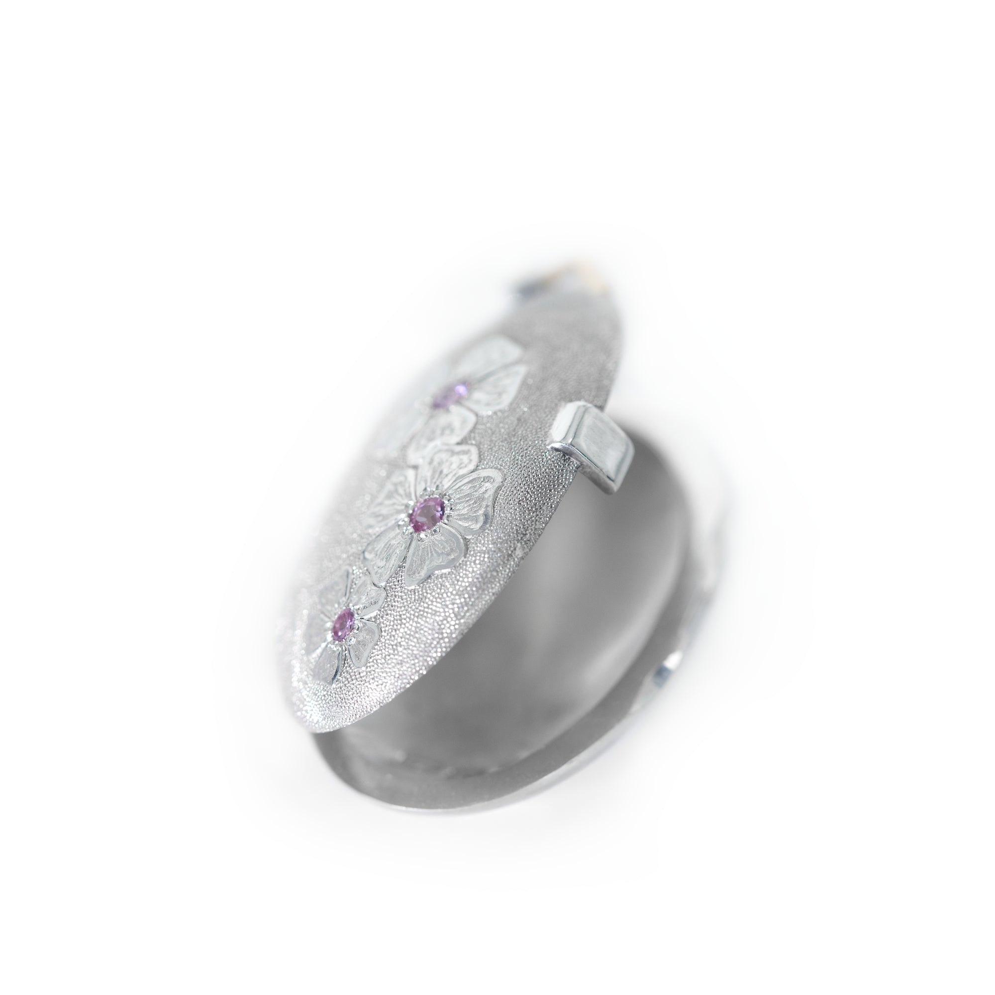 Bright silver locket adorned with hand engraved cherry blossom flower with pink sapphires is open and presented on the white background. Locket by Ewa Z. Sleziona Jewellery