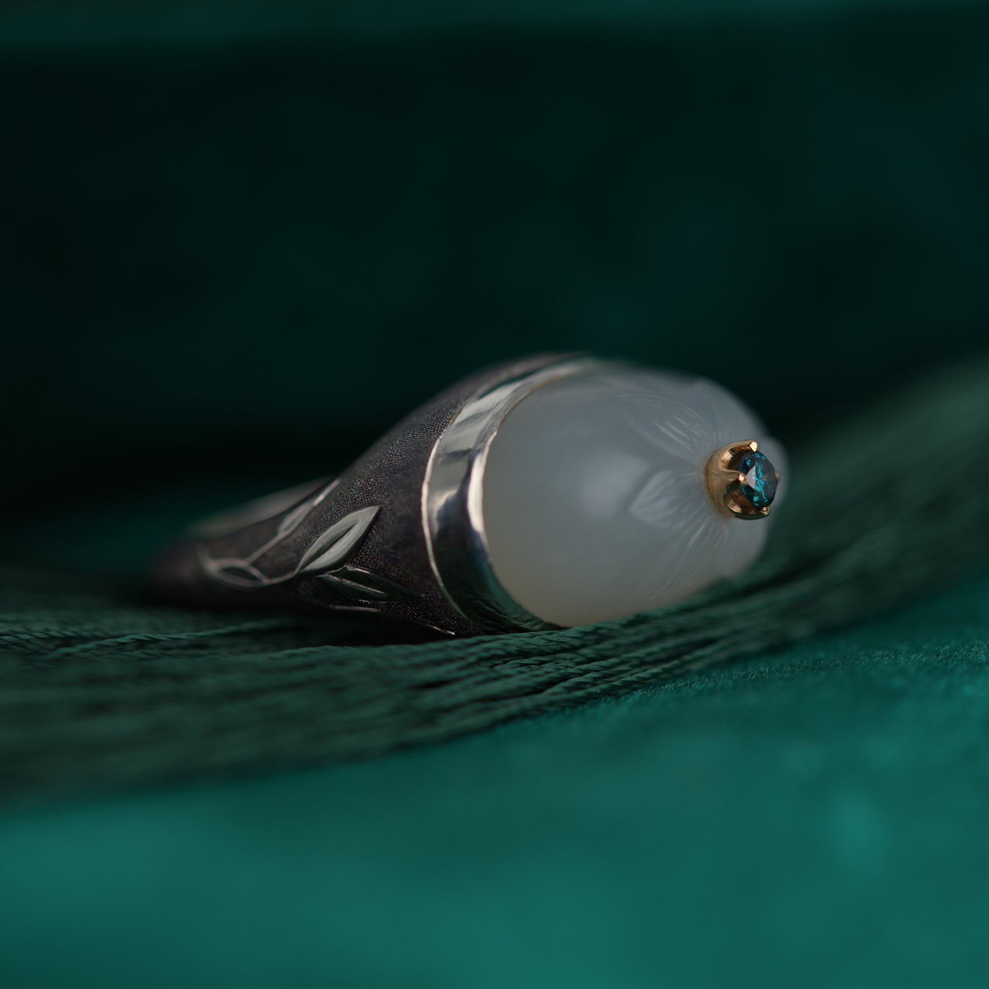 Ring with grey cameo and blue gemstone with intricate designs on a green fabric background