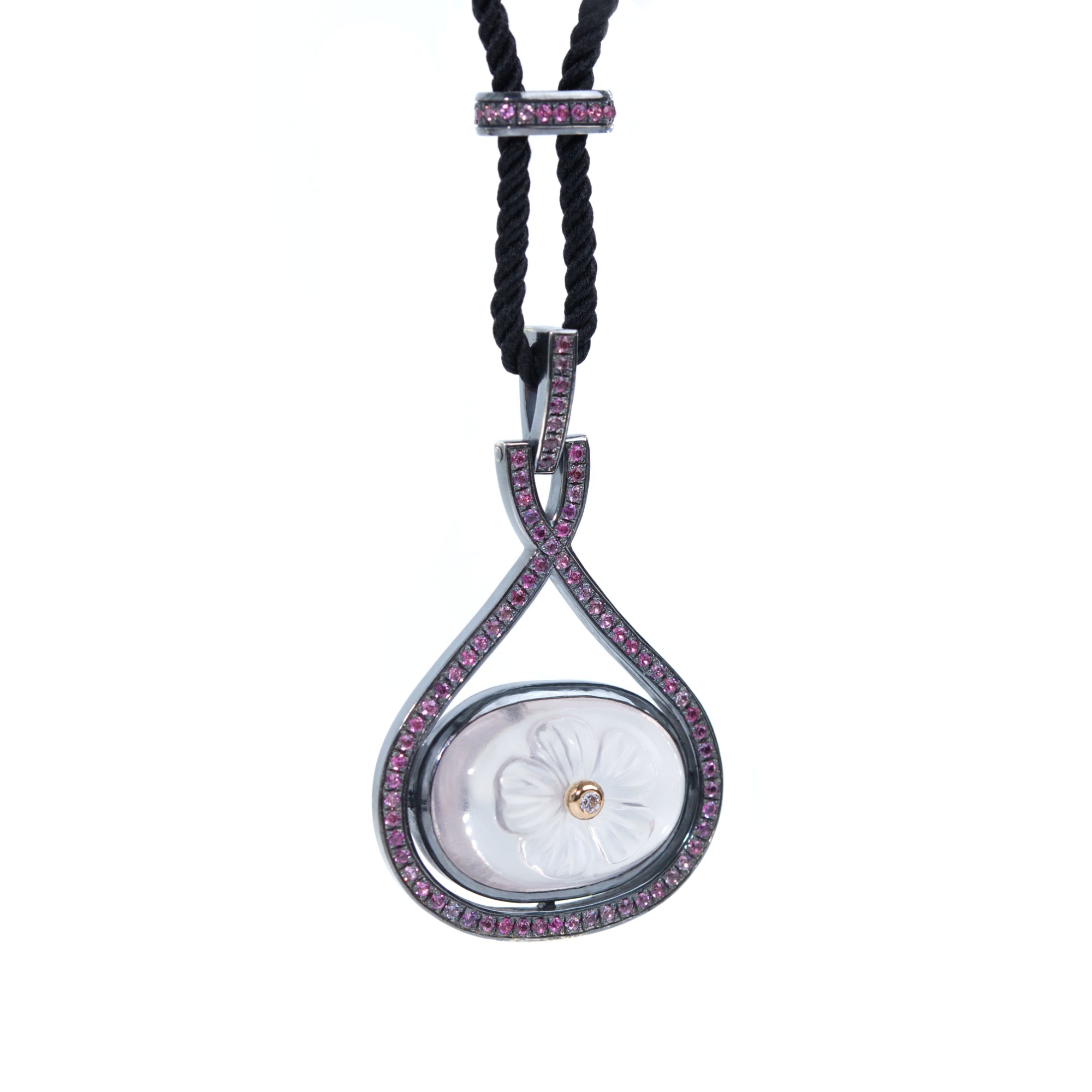 A necklace featuring carved rose quartz adorned with white diamond hangs from black rope. The necklace is presented on white background.