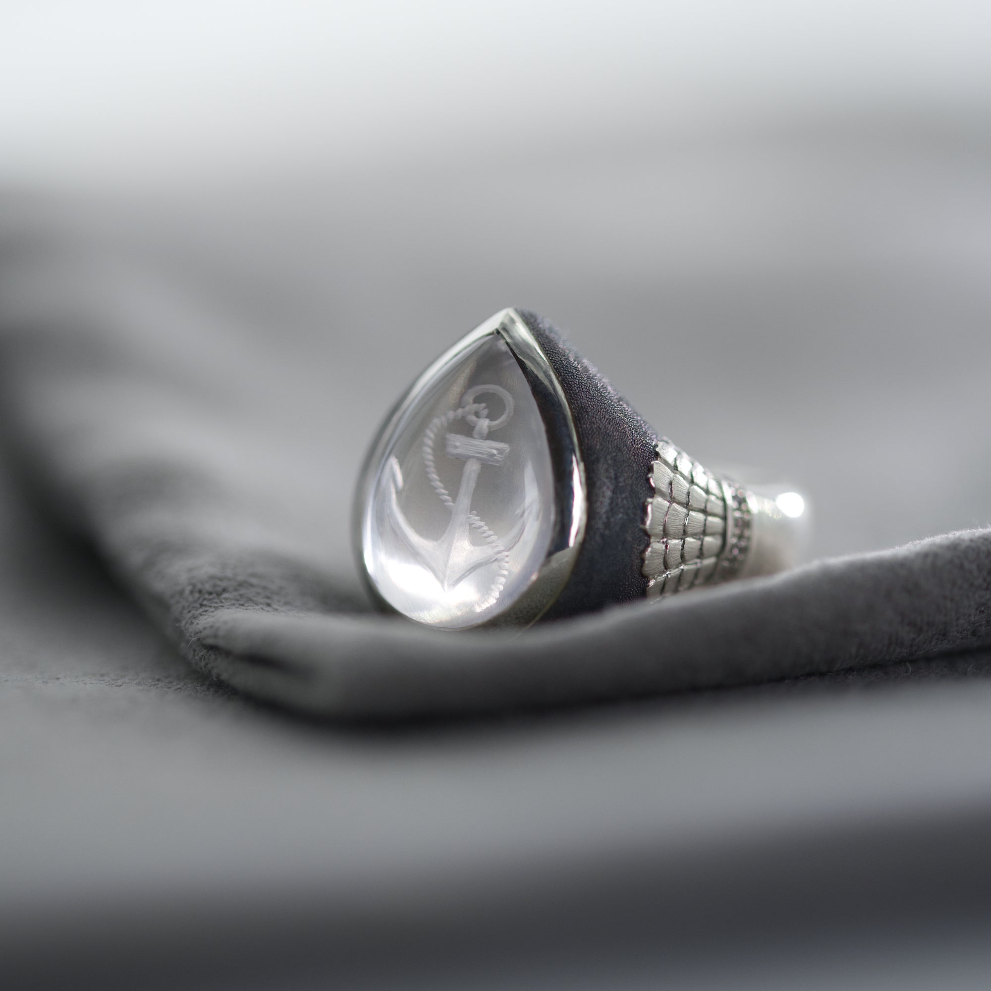 Teardrop-shaped silver ring with engraved design on a gray fabric background