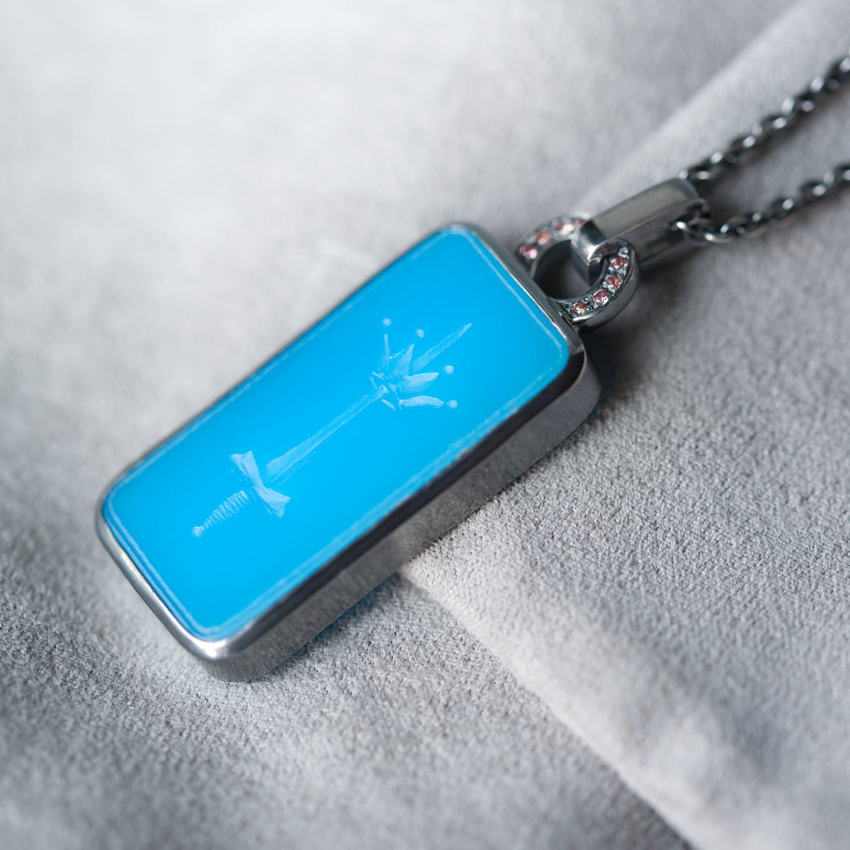 Intaglio necklace in blue featuring carved sword and crown. Pendant is adorned with peach-pink sapphires. the piece is made of blackened silver and showcased on grey background.