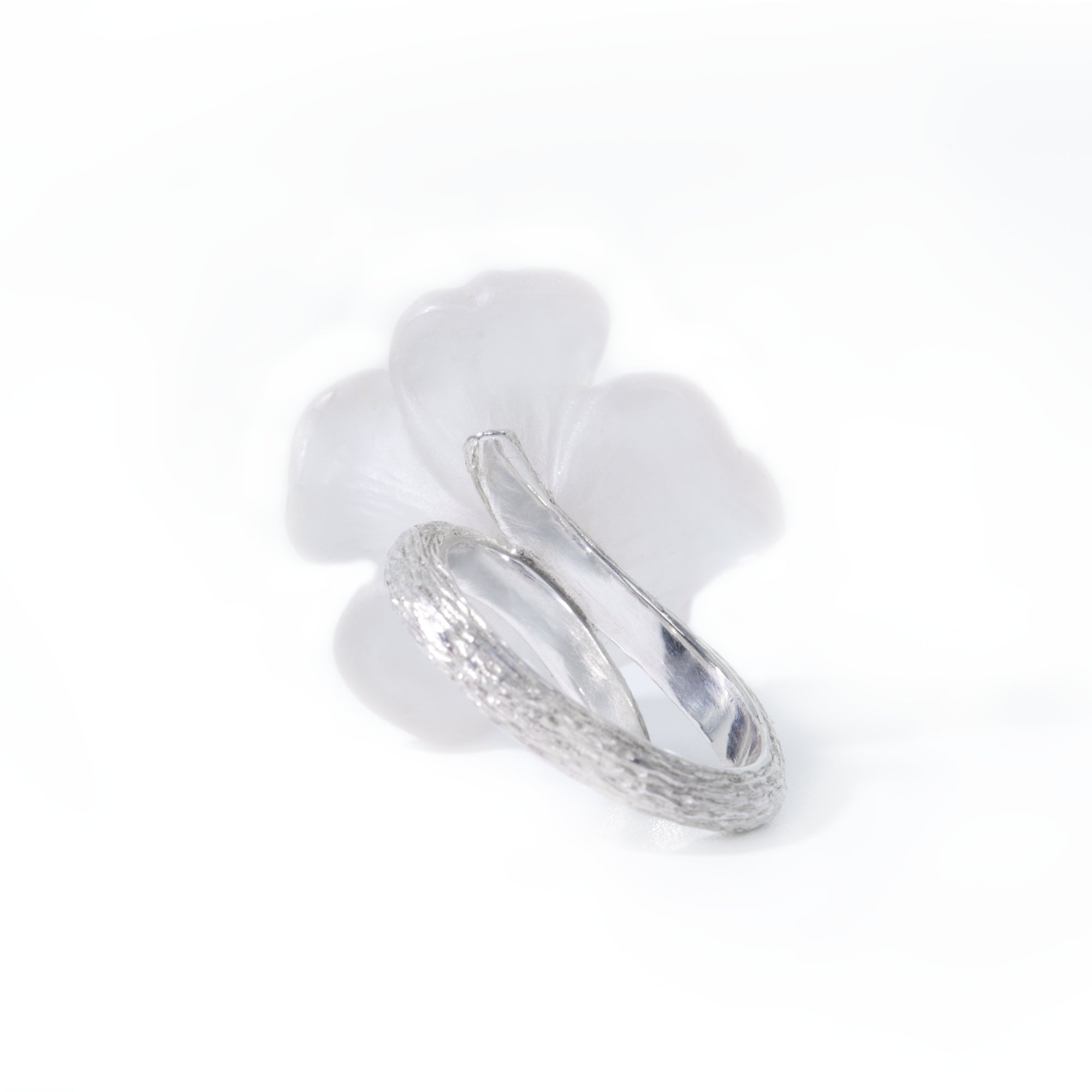 Photo shows a back of the white pansy flower ring carved in rock crystal and its silver band presented on white background.