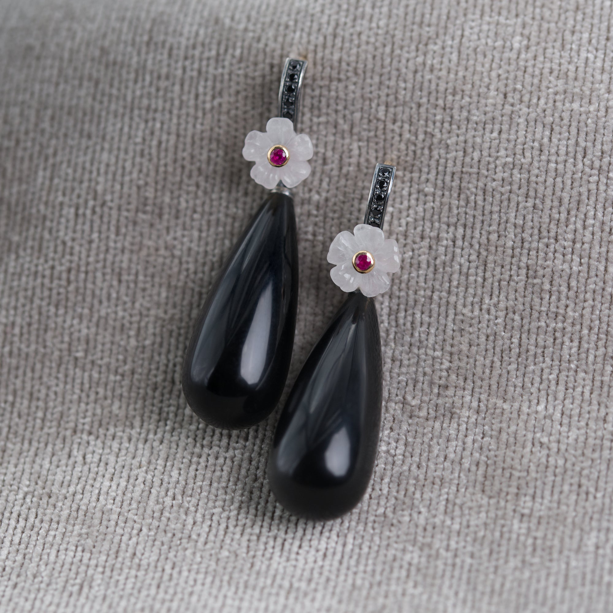 Black teardrop earrings with floral tops and gemstones on a textured gray surface