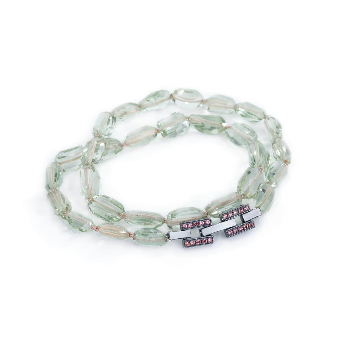 The photo shows a green prasiolite necklace, hand-knotted. The necklace's clasp is made of blackened silver and decorated with pink-peach sapphires.