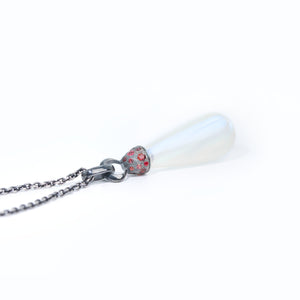 Moonstone necklace adorned with blackened silver cap with  red sapphires is lying on white background.