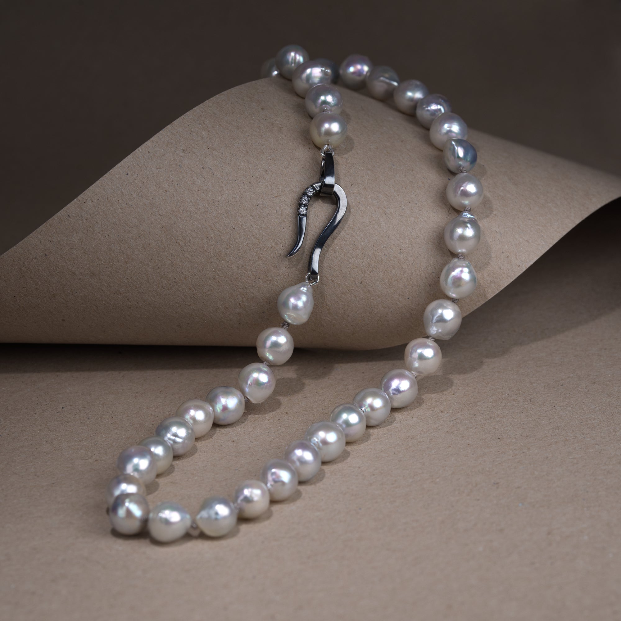 The necklace is presented on a natural background. Necklace composed of gray pearls with a highlighted clasp.