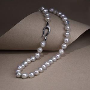 The necklace is presented on a natural background. Necklace composed of gray pearls with a highlighted clasp.