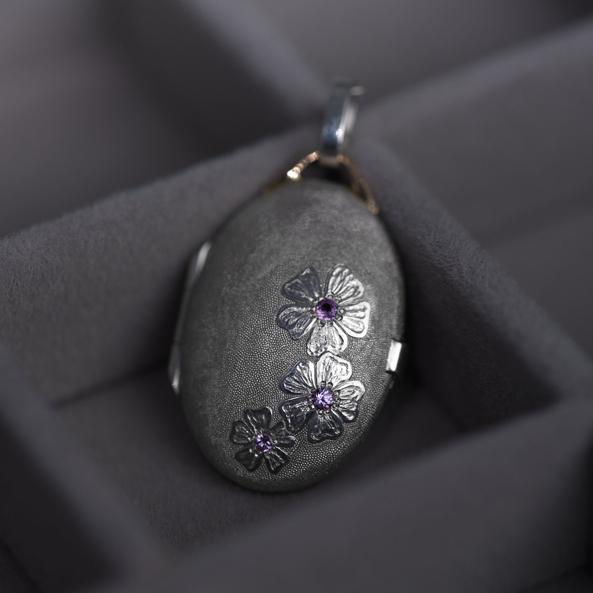 Bright silver locket with 18K gold details and hand engraved cherry blossom flowers adorned with pink sapphires is presented on the grey background. Locket by Ewa Z. Sleziona Jewellery