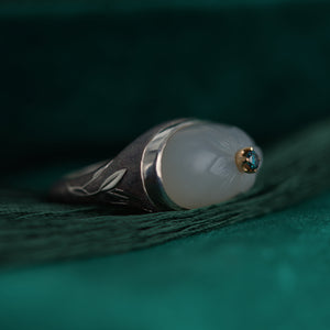 Ring with grey cameo and blue gemstone with intricate designs on a green fabric background