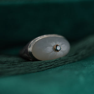 Close-up of a silver ring with a blue central gemstone on a textured green surface