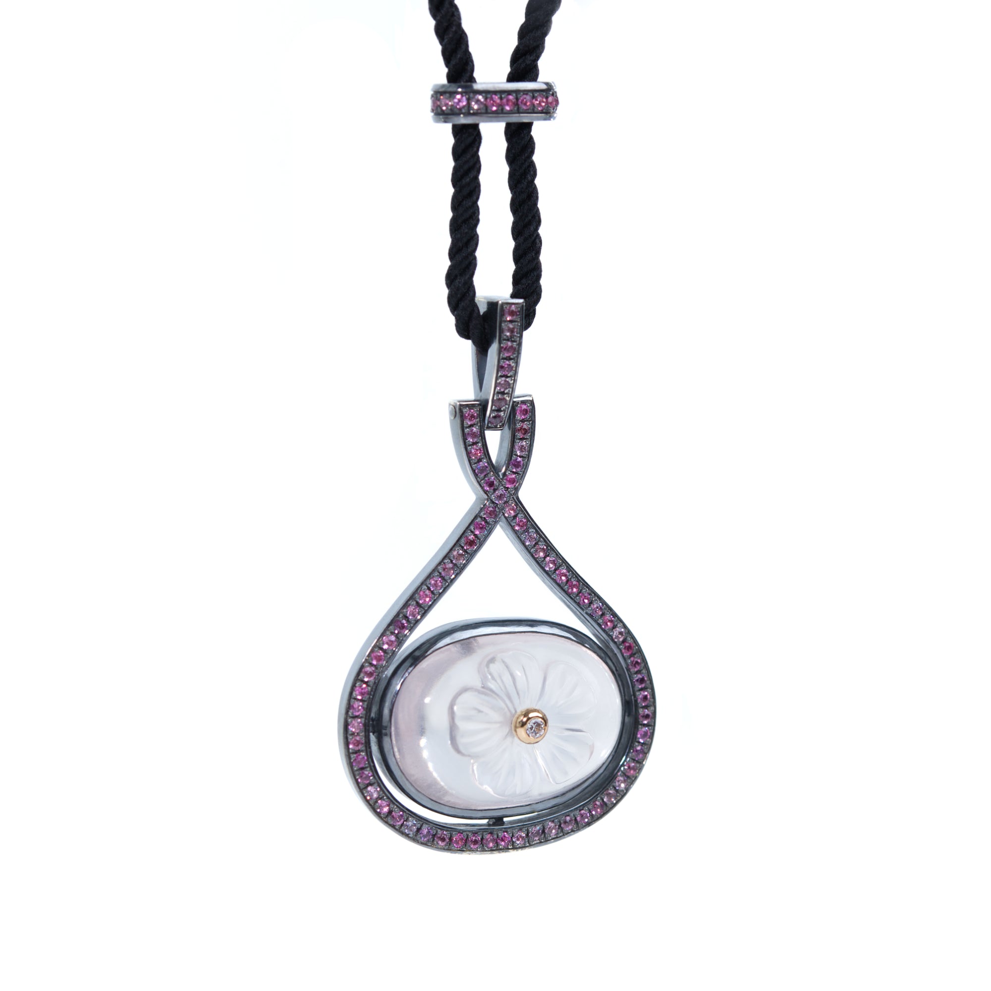 A necklace featuring carved rose quartz adorned with white diamond hangs from black rope.  The necklace is presented on white background.  