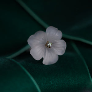 White pansy flower ring carved in rock crystal and adorned with chocolate diamond presented on green velvety background.