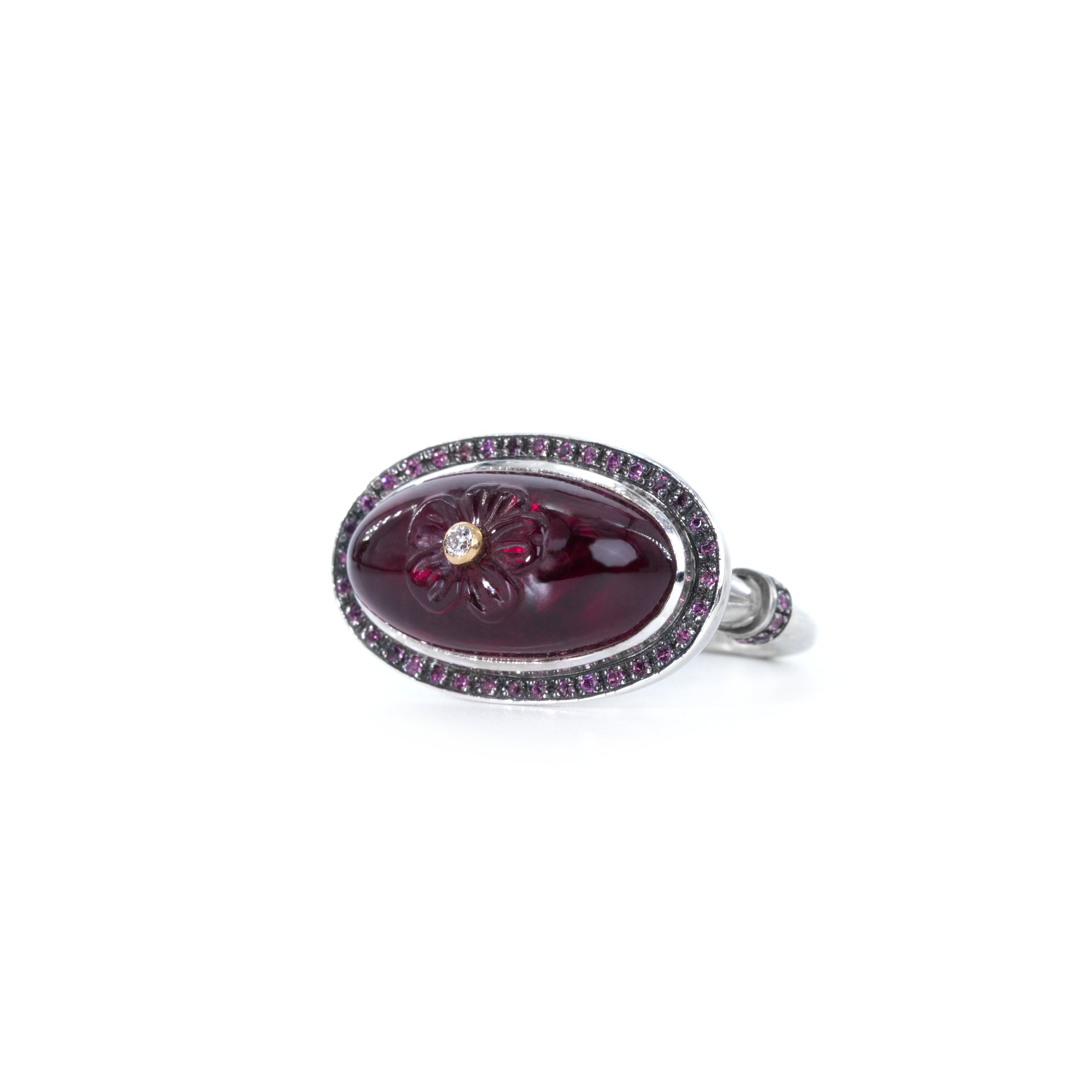 Sterling silver ring with oval rhodolite cabochon. The gemstone is hand carved with flower and adorned with white diamond set in 18K gold. The ring's crown is finished with halo of rhodolites