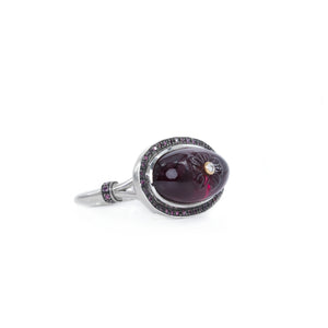 Sterling silver ring with oval rhodolite cabochon features the right side of the ring. The gemstone with hand-carved flower and white diamond. The shank of the ring is split and adorned with rhodolites.