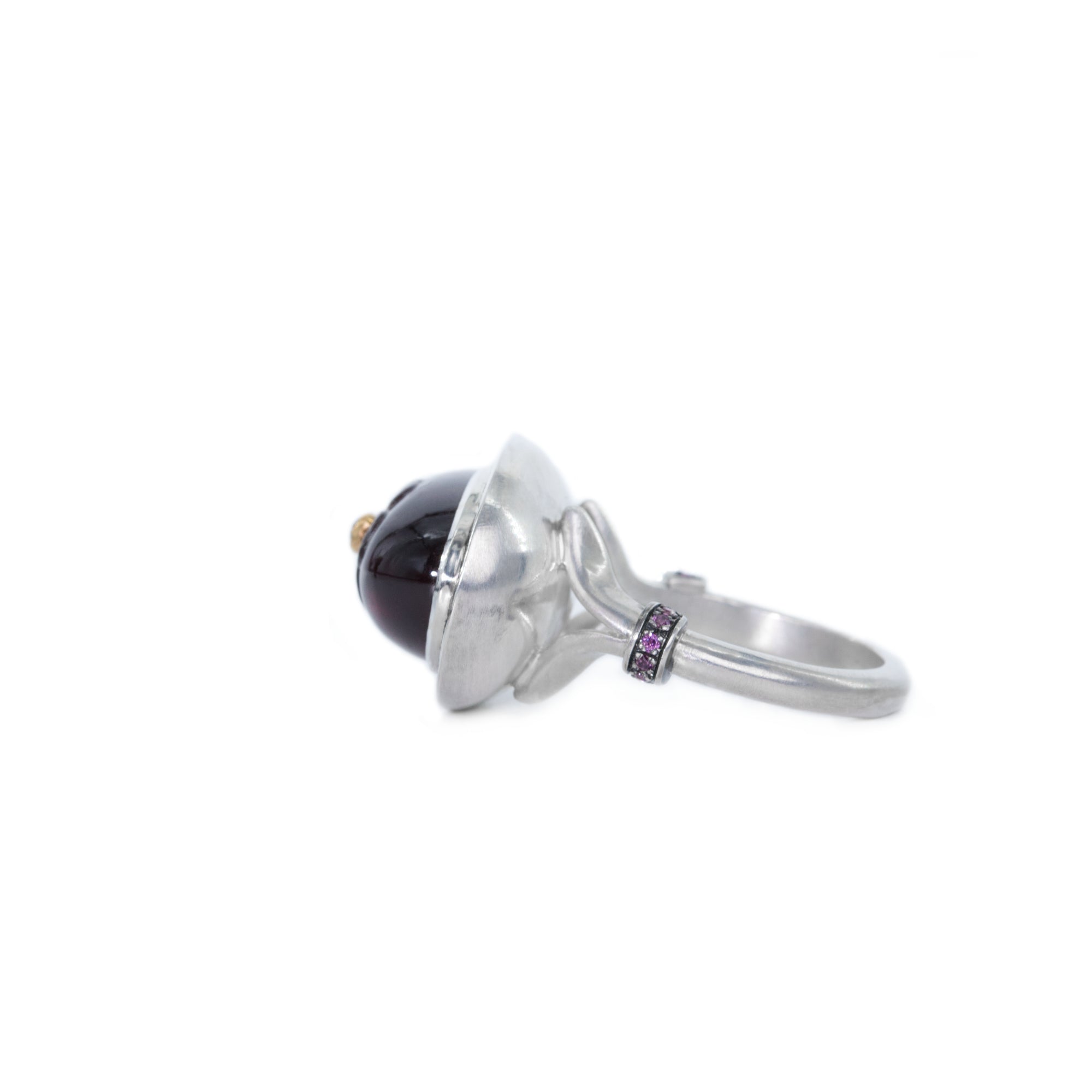 Sterling silver ring with oval rhodolite cabochon features the right side of the ring. The gemstone with hand-carved flower and white diamond. The shank of the ring is split and adorned with rhodolites.