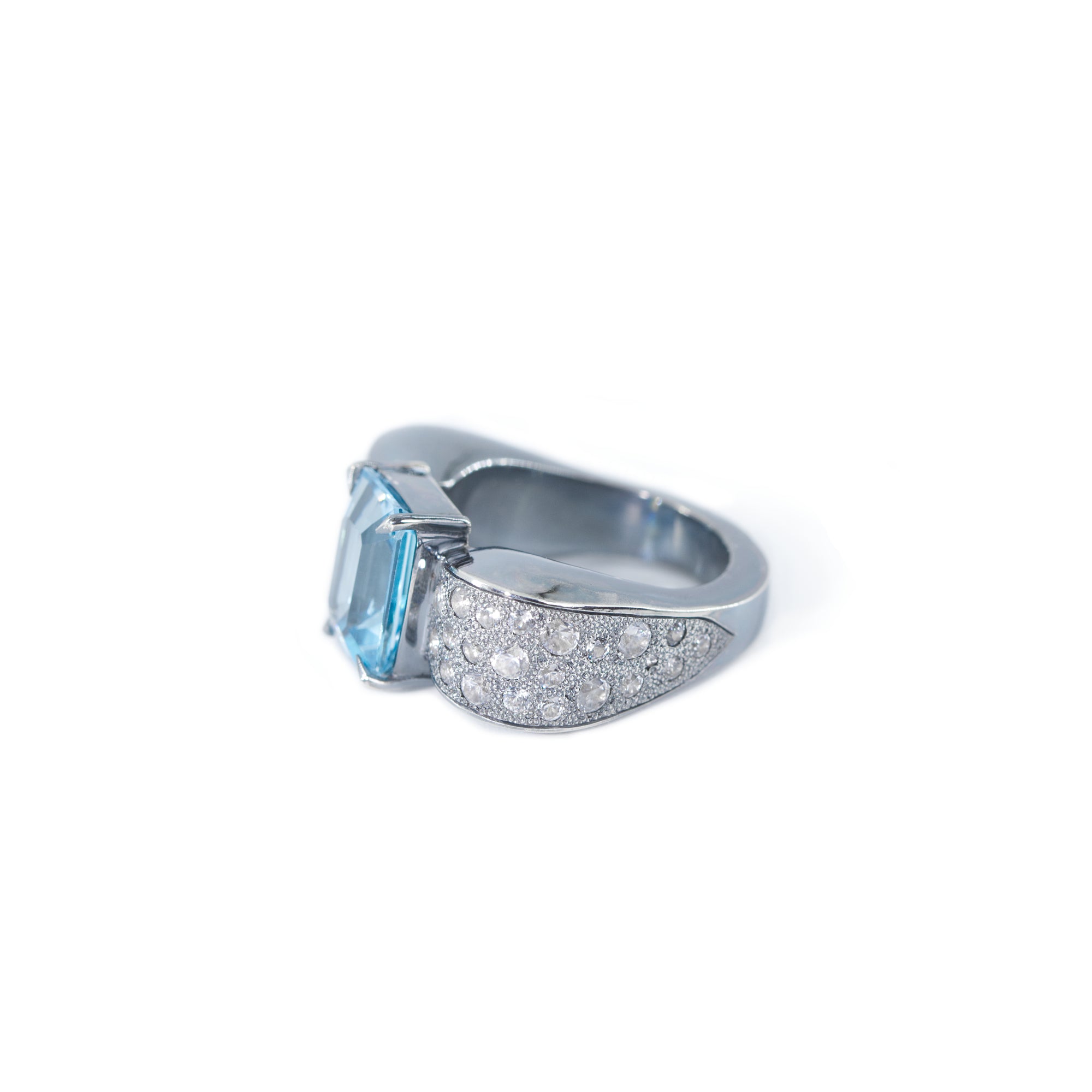 The photo shows a side view of the bow-shaped ring. In the center of the bow there is an octagonal blue topaz, the side of the bow is decorated with round white zircons.