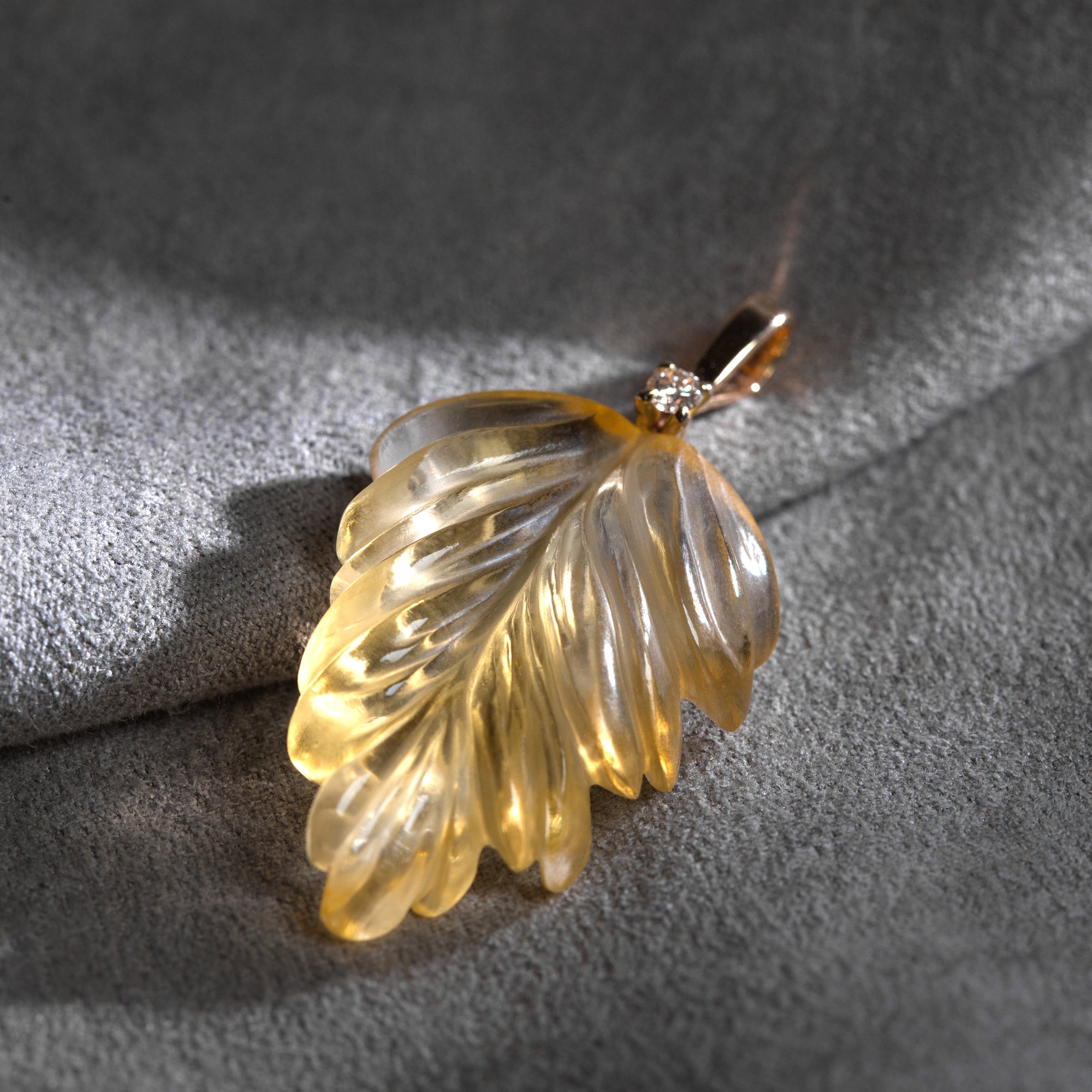 The photo presents hand-carved citrine leaf placed on grey background. The leaf is finished with light brown diamond and 18K gold stem.