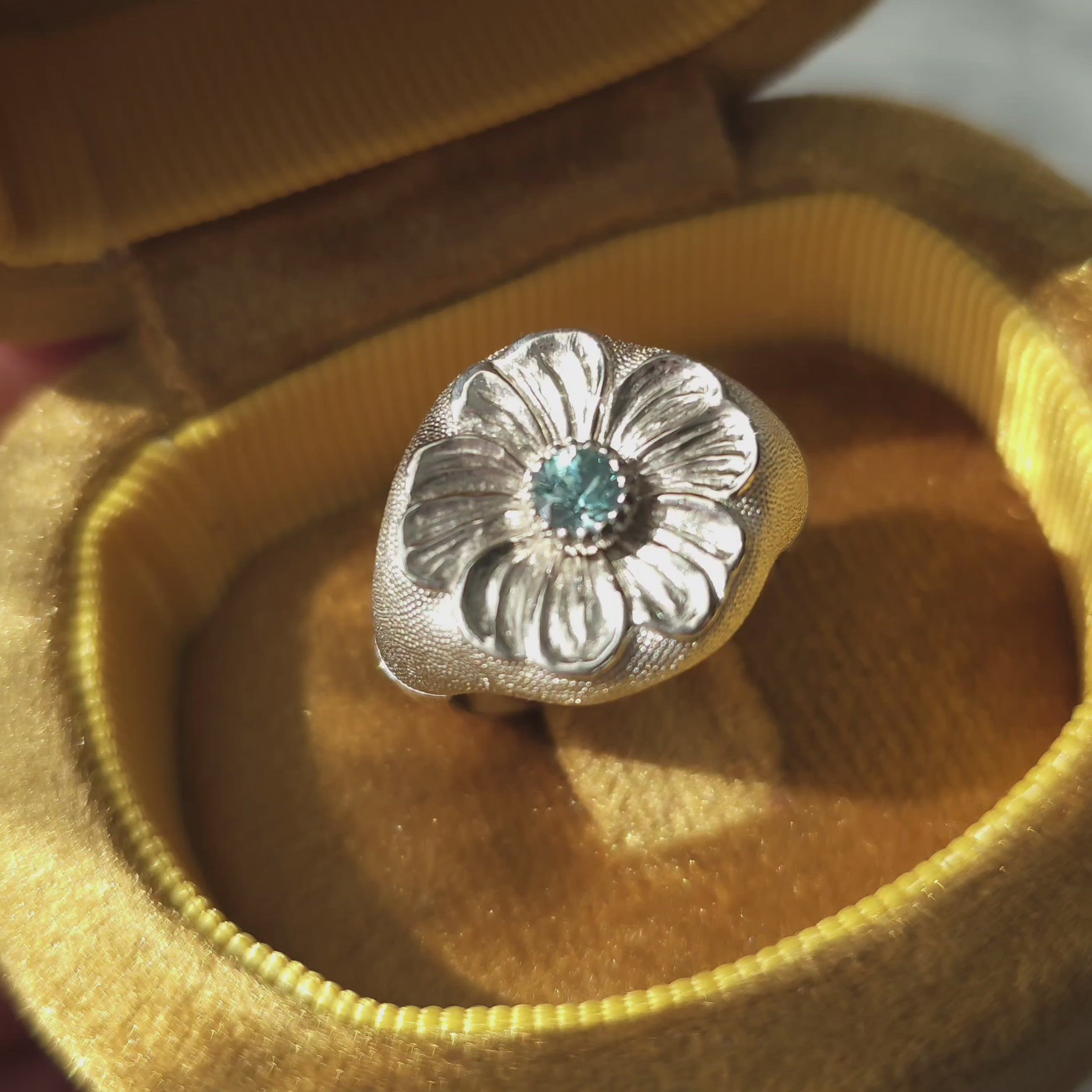 A short video presenting flower signet ring with blue gemstone in golden jewellery box.